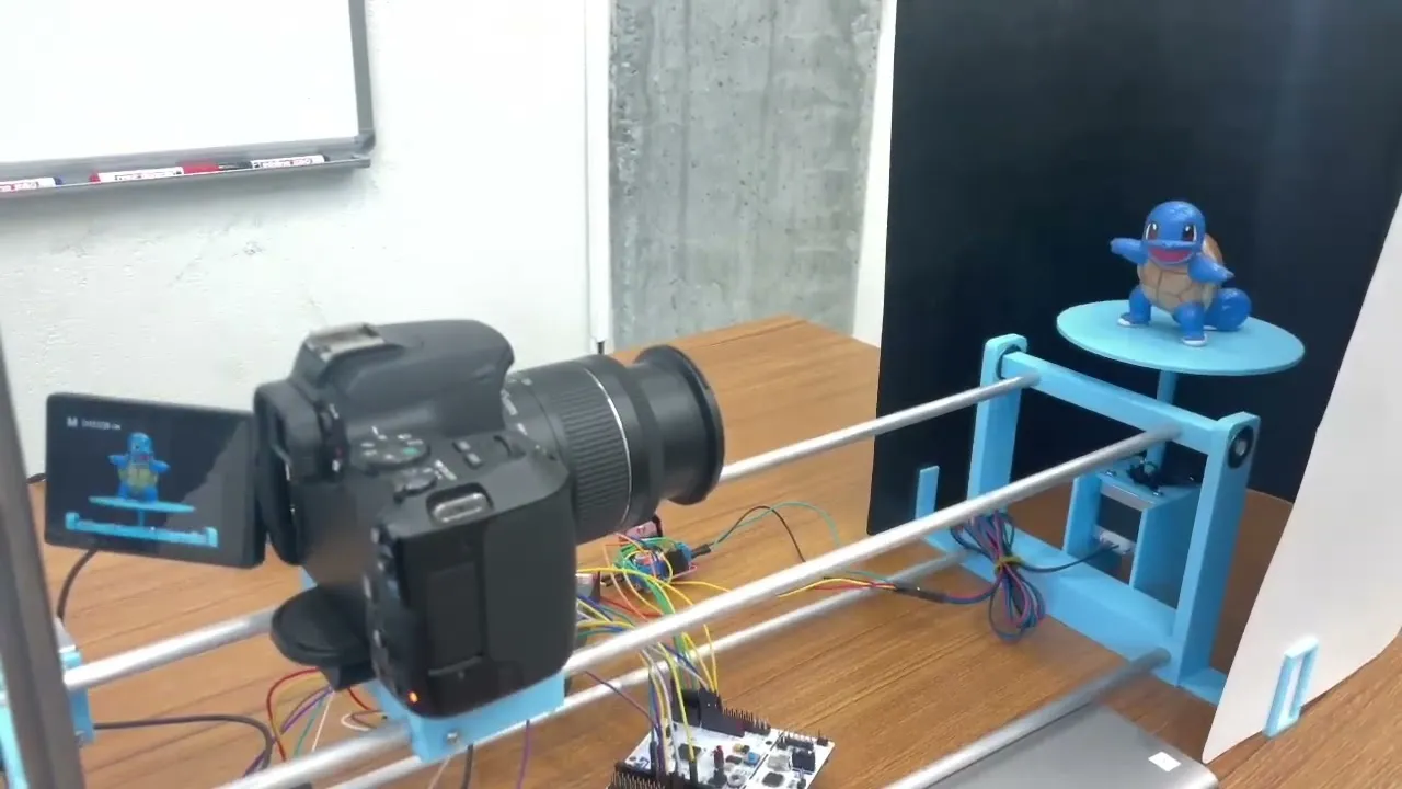 3D scanner rig: a DSLR camera on a blue 3D-printed rail facing a figurine on a motorized turntable